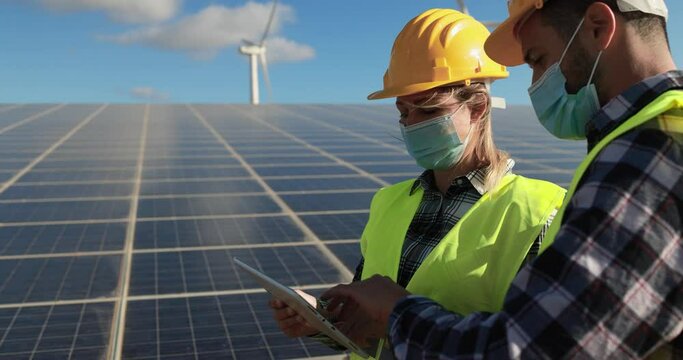 Working people with digital tablet  wearing safety masks - Solar panels with wind turbines generating electricity - Alternative renewable energy from nature - Ecology concept