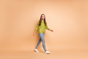 Fototapeta na wymiar Full length photo of girl walk go look camera wear green sweater sneakers jeans isolated beige color background