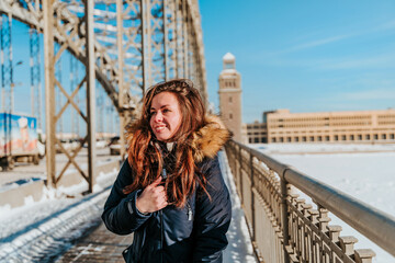 A young woman in a jacket walks on a snow bridge in St. Petersburg in winter in sunny weather