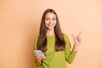 Photo of funny girl hold phone direct finger empty space wear green pullover isolated beige color background