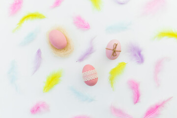 Ester composition with colorful eggs and pastel feathers on white background. Flat lay