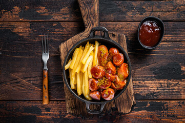Currywurst street food meal, Curry spice on wursts served French fries in a pan. Dark wooden...