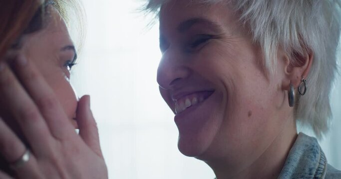 Cinematic shot of carefree happy homosexual female gay and transgender man couple in love is enjoying time together is hugging and kissing with affection as sign of timeless forever love at home.