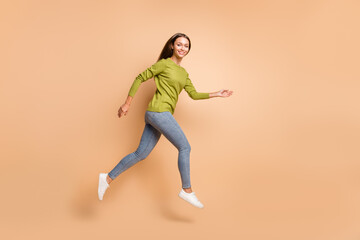 Fototapeta na wymiar Profile photo of energetic girl jump go wear green sweater jeans sneakers isolated beige color background