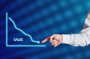 Businessman hand points to the word sales with a decreasing chart or graph.