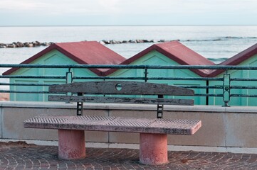 A concrete and wooden bench on the sidewalk in front of beach cabins on the Mediterranean coast (Pesaro, Italy, Europe)