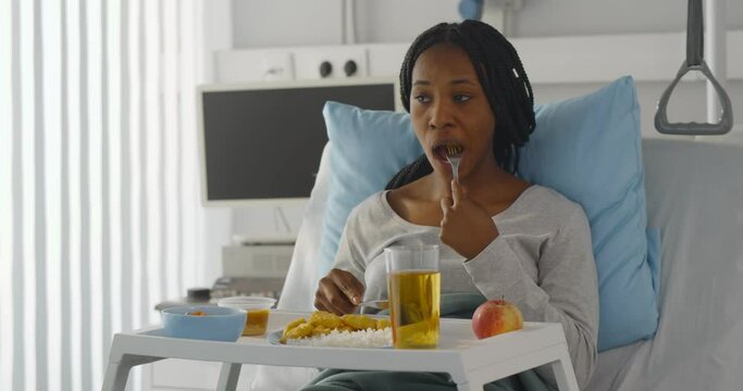Afro-american young woman patient eating lunch on tray in hospital bed