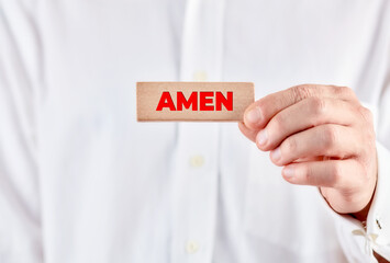 Male hand showing a wooden block with the word Amen.