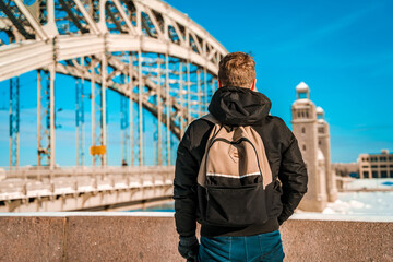 A young man in a jacket walks on a snow bridge in Saint Petersburg in winter in sunny weather