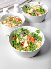Fruit salad with strawberries, pineapple pieces, herbs, red onions and cheese in white ceramic bowls on a light background. Ideas and recipes for a healthy diet. Vegeterian food. Vertical shot