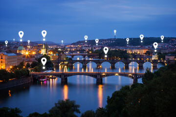 Map pin icons on Prague cityscape. Lit buildings and bridges over Vltava River in Prague, Czech Republic, at dusk.