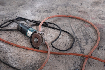 A grinding machine which is using to cutting the metal and grind metal object that placed on the concrete floor with messy electric cable line. Close-up and Selective focus at the equipment part.