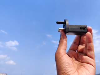 Human hand holding black color smart phone USB charger. Cloud background