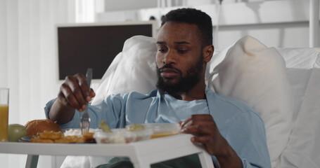 African male patient in hospital bed eating meal from tray