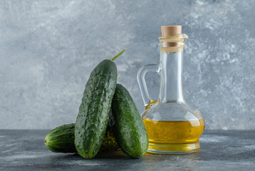 Pile of cucumber with bottle of oil over grey background