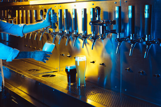 Young man bartender pouring lager beer from tap to glass in neon light.