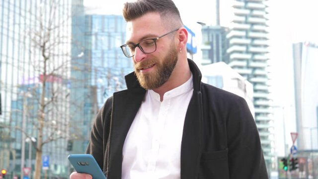 Slow motion young caucasian bearded business man outdoor using smartphone handhold stopping and staring at the camera