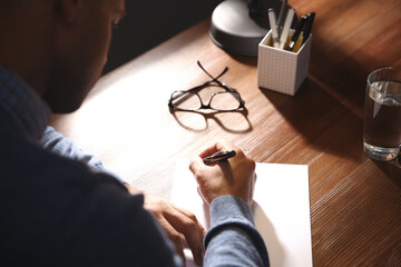 Man writing letter at wooden table indoors, closeup