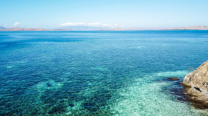 A drone shot of a paradise island in Komodo National Park, Flores, Indonesia. Brownish island turns into white sand beach and further into turquoise and navy blue sea. Steep slopes of the island