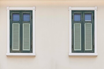 Two vintage green shuttered wooden windows and cream colored facades
