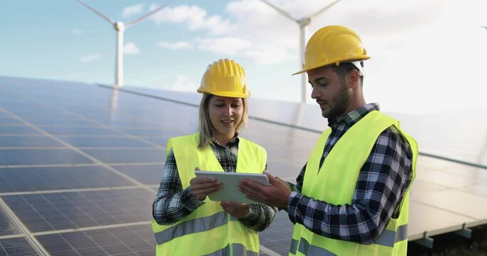 Young people working with digital tablet at solar panels station and wind turbines generating electricity - Alternative renewable energy concept