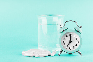 Alarm clock, a glass of water and white capsules with biological active additives or vitamins on a...