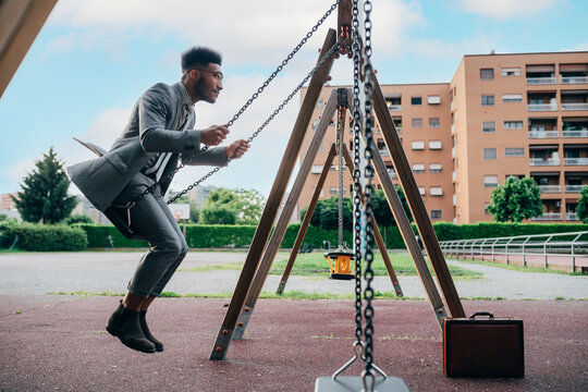 Young adult business man sitting alone in a playground swinging on a seesaw