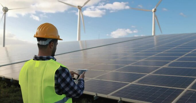 Young man working with digital tablet - Solar panels with wind turbines generating electricity - Alternative renewable energy concepy