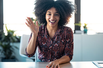 Beautiful afro young woman waving hand while doing video call looking at camera in the office.