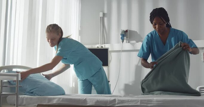 Diverse young nurses making bed and cleaning in hospital ward