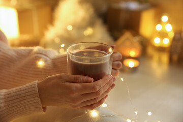 Woman with cup of drink and blurred Christmas lights on background, closeup
