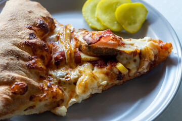 A slice of potato pizza and some pickles on a gray plate on a white marble table.