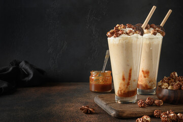 Tasty banana and caramel milkshake garnished whipped cream and popcorn on dark brown background.