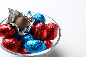 Glass bowl with chocolate eggs wrapped in colorful foil on white background, closeup