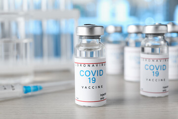 Glass vials with COVID-19 vaccine on wooden table