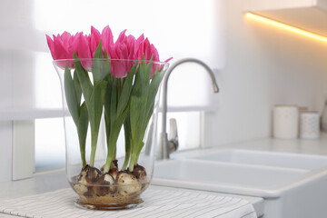 Bouquet of beautiful tulips with bulbs on countertop in kitchen. Space for text