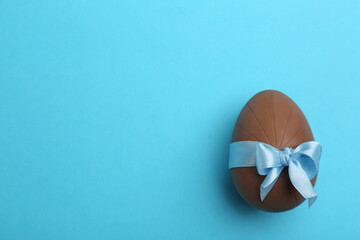 Sweet chocolate egg with bow on light blue background, top view. Space for text