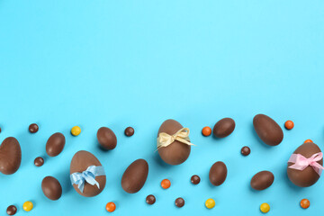 Sweet chocolate eggs and bright candies on light blue background, flat lay. Space for text