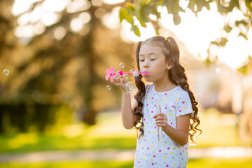 Cute little Asian girl in the summer on a walk blowing soap bubbles