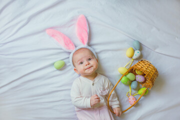 Fototapeta na wymiar Cute funny baby with bunny ears and colorful Easter eggs at home on a white background
