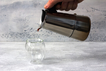 Filling a coffee in a thermos glass shot out of geyser coffee maker on a light gray textured...