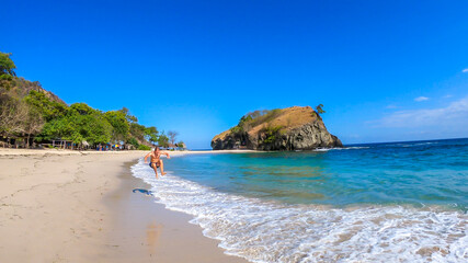 Fototapeta premium A man jumping into the waves on idyllic Koka Beach. Hidden gem of Flores, Indonesia. He is having a lot of fun, collecting happy moments. Adventure and discovering while travelling
