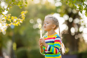 Cute little girl on a walk in a multi-colored knitted blouse in a striped summer blowing soap bubbles