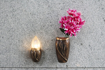 A small light glowing and a vase with plastic flowers on the exterior of a granite tomb wall. Small...