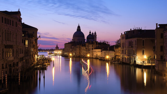 Romantic Venice at night. Cityscape image of Grand Canal in Venice, with Santa Maria della Salute Basilica reflected in calm sea. Lights of passenger boat on the water.