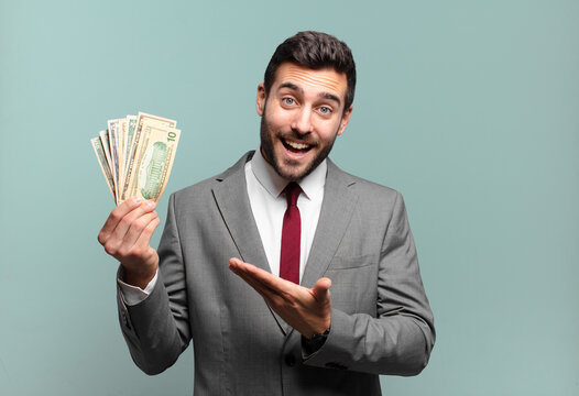 young handsome businessman smiling cheerfully, feeling happy and showing a concept in copy space with palm of hand. bills or money concept
