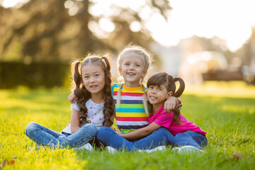 Fototapeta premium three little girls cuddle in the summer on the lawn. International Children's Day