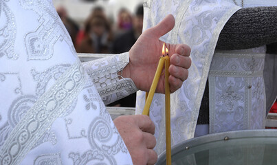 An Orthodox priest covers a candle flame with his hand from the wind. Consecration of water. The...