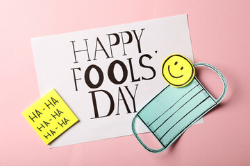 Paper mask and Happy Fools' Day note on pink background, flat lay