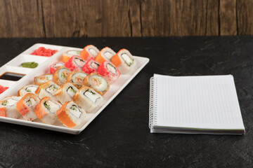A white board of different types of delicious sushi rolls with notebook